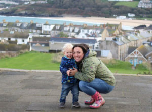 Katy and Max crouching down in lighthouse clothing coats, in St Ives Cornwall