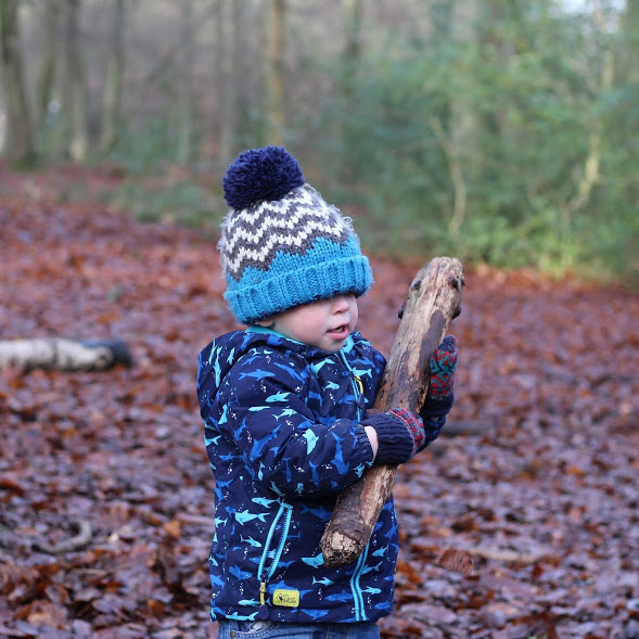 Max carrying huge log in woods with woolly hat fallen down over his eyes