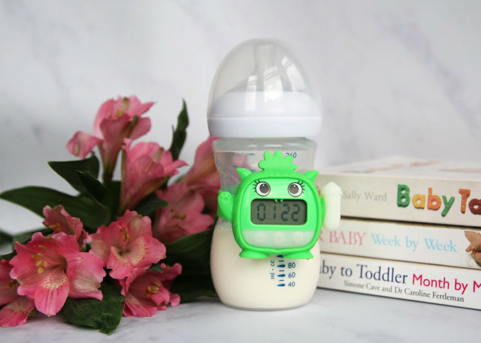 Bottle with Milk Monster attached, next to pink flowers and stack of parenting books