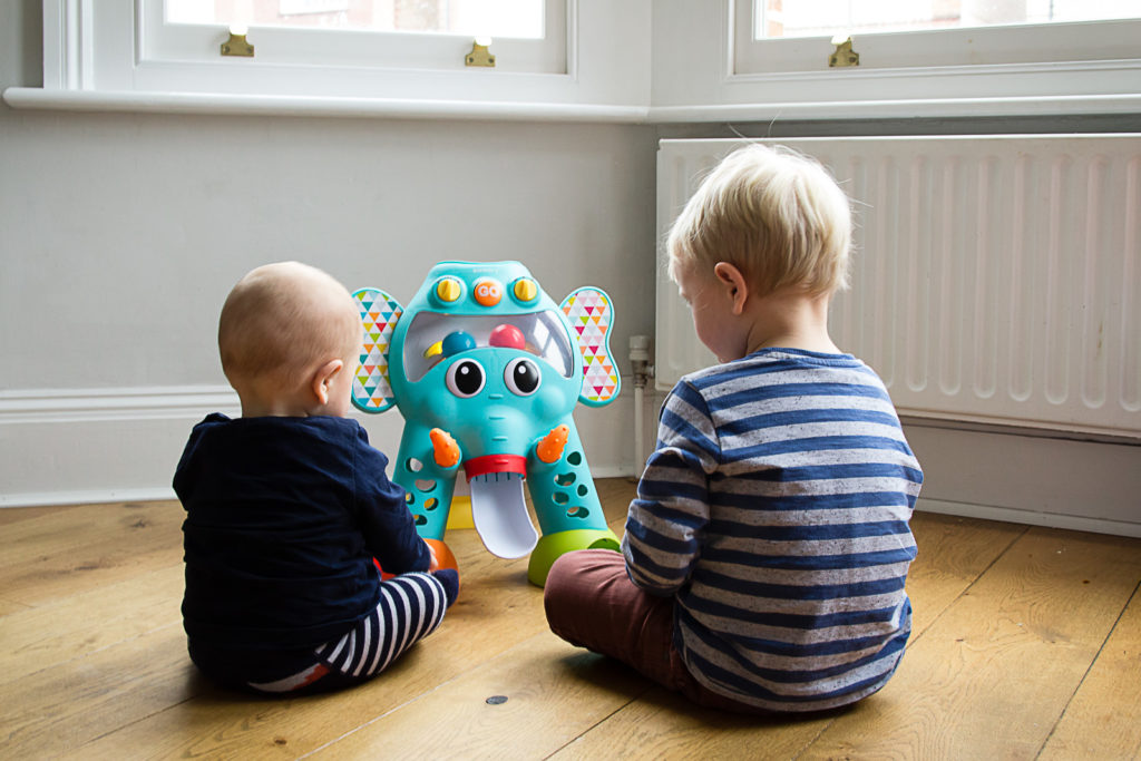 Two boys, aged 3 and 9 months, sat in front of the Infantino Cruise Around Activity Elephant, with backs to the camera, playing together, feeding the balls into it