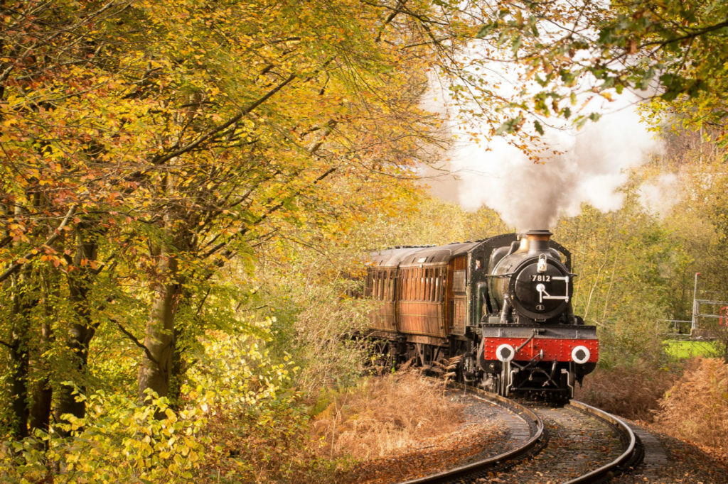 Steam train coming around a bend, with autumnal trees in the foreground