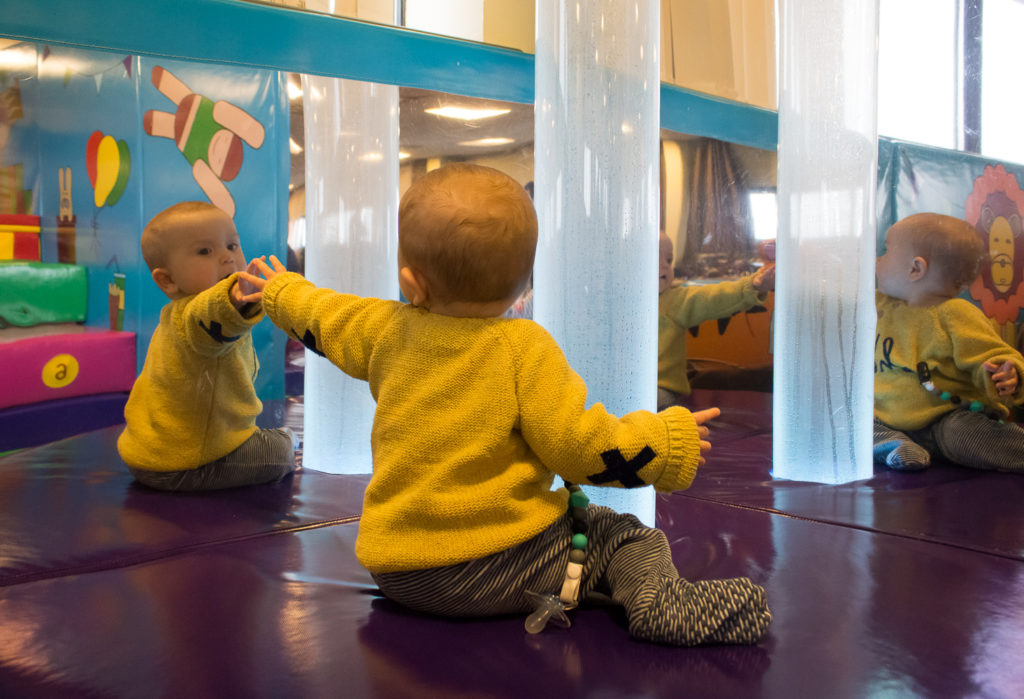 Sensory area for babies in the Circus Room at Bluestone Wales. A baby dressed in yellow jumper is reaching to touch his reflection in the mirror