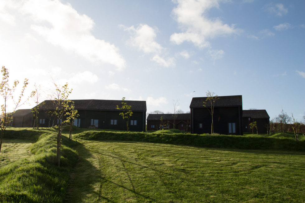 Lodges at Bluestone Wales, with blue skies above and fluffy white clouds, and green grass