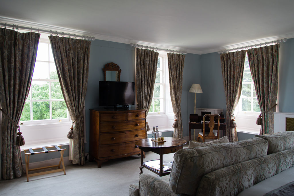 Bedroom at Chicheley Hall hotel, with pale blue walls, windows overlooking the grounds, and dark wood chest of drawers