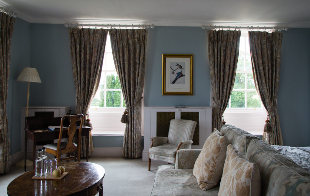 Bedroom at Chicheley Hall hotel, with two Georgian panelled windows overlooking the grounds, with sweeping curtains