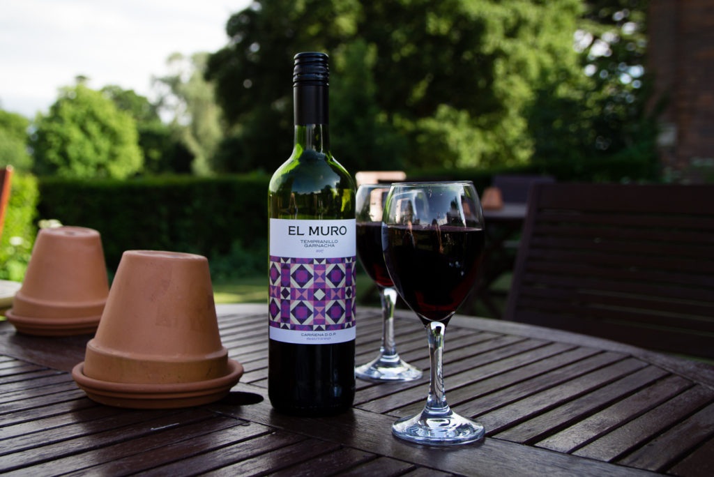 Bottle of red wine and two glasses filled with wine, on table outside in a garden