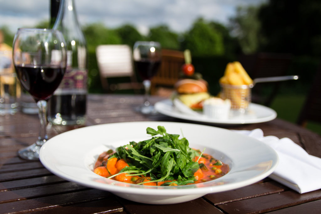 Tomato gnocchi at Chicheley Hall hotel. Bowl placed on table outdoors in a garden, with glass of wine behind it