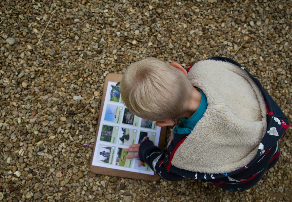 Little boy looking at clipboard with checklist which is placed on the ground on gravel pathway