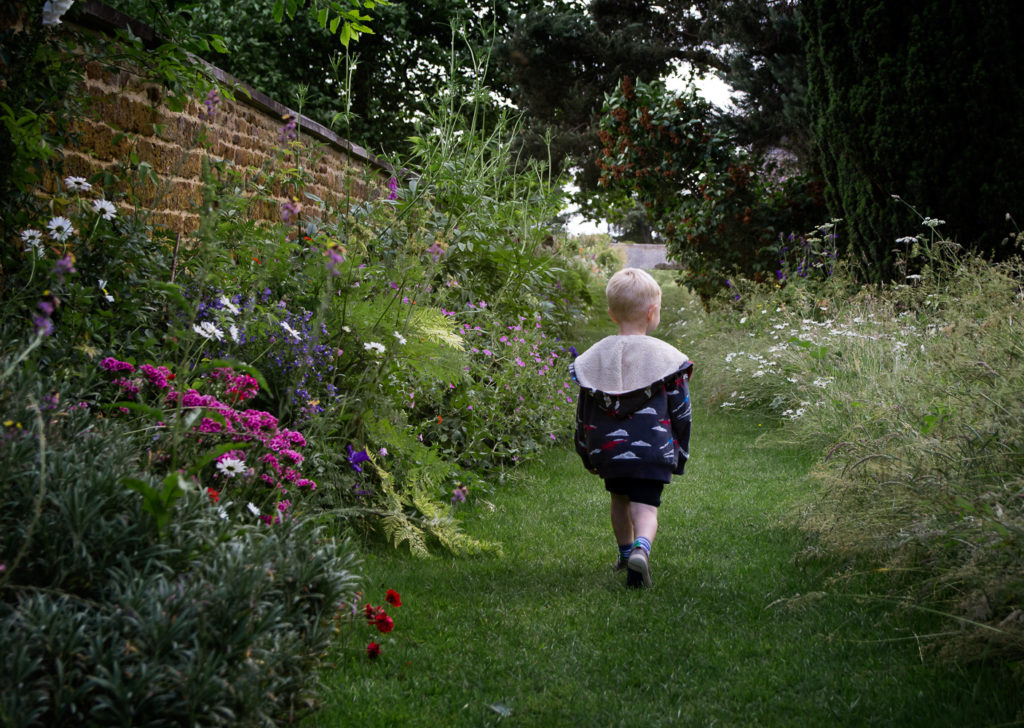 Little boy walking down a pathway through the borders at Canons Ashby National Trust