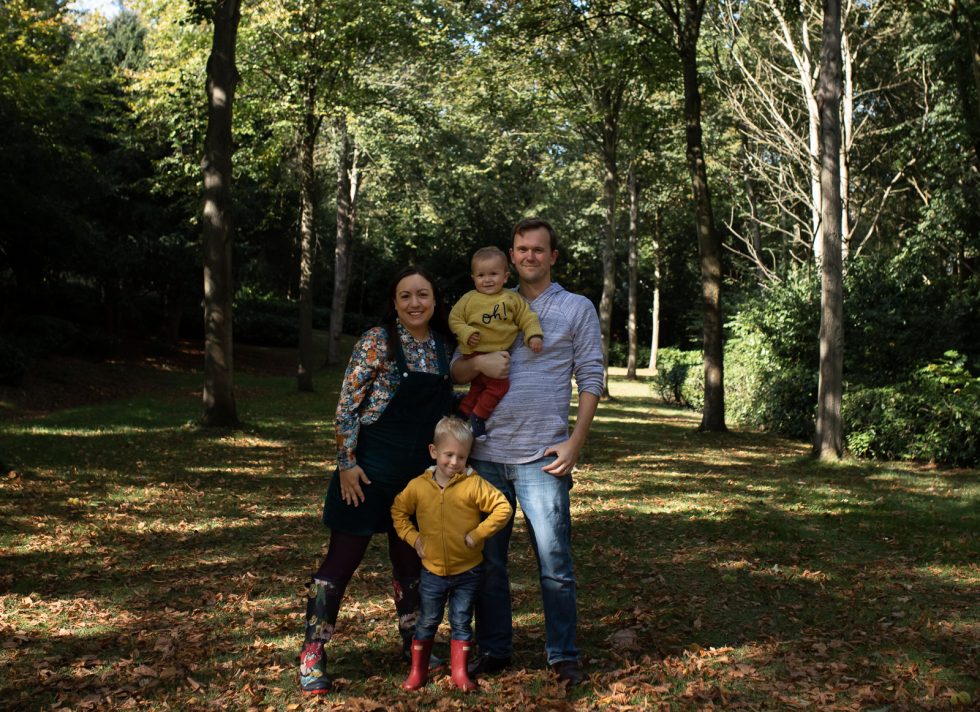 Family standing in dappled sunlight in the woods, with autumn leaves on the ground