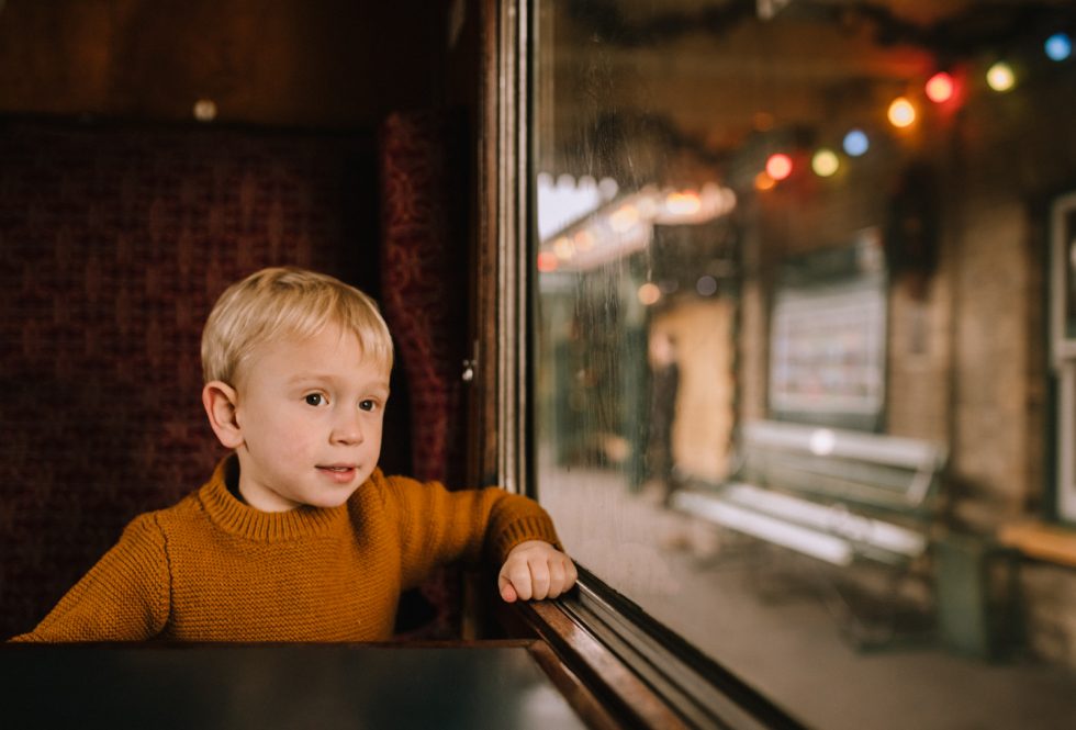 Little blond boy, sat on train, looking out of the window