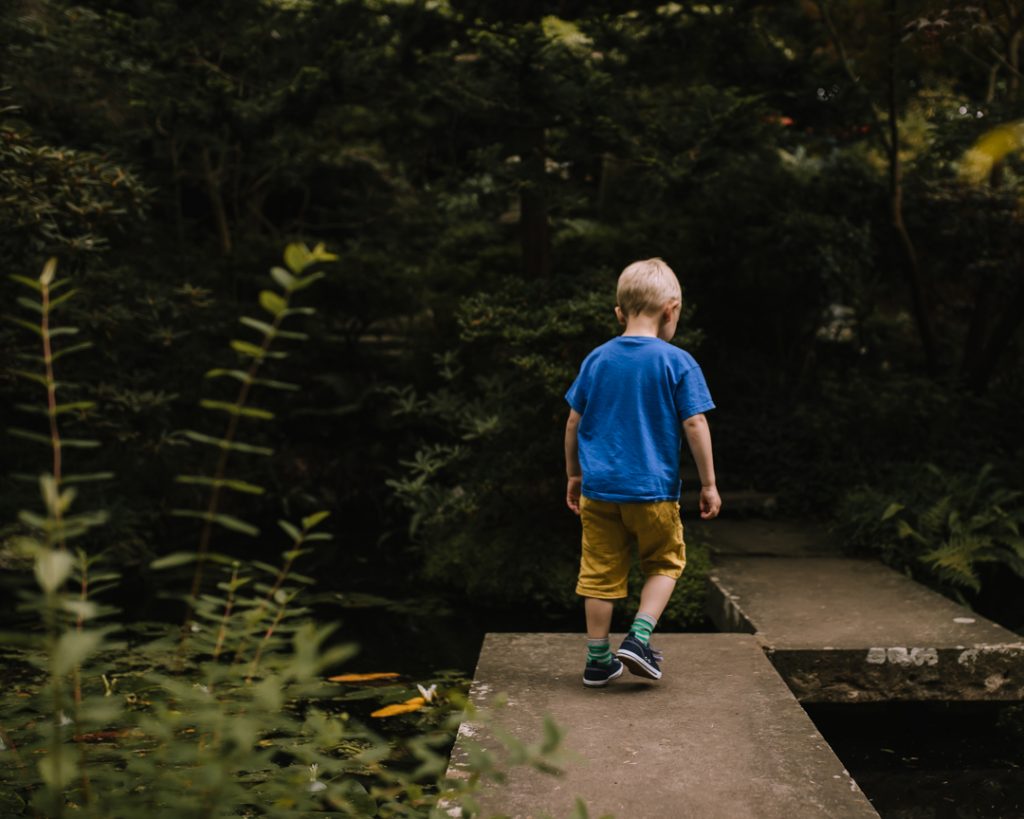 Little boy walking across concrete walkway over pond in the Japanese garden at Compton Acres